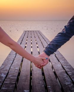 Cropped image of people holding hands walking on pier against sky