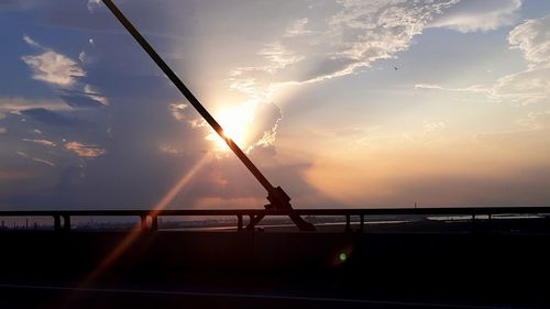 Silhouette railing by sea against sky during sunset