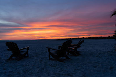 Chairs on beach against sky during sunset