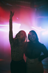 Portrait of happy young female friends standing with arms around at nightclub