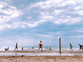 People playing on beach against sky