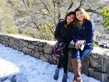 Portrait of smiling friends sitting on retaining wall