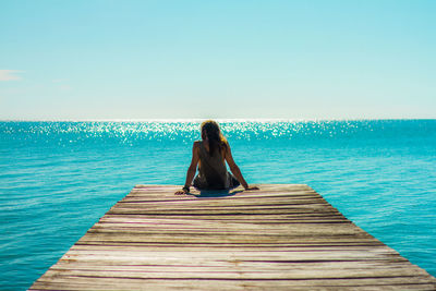 Rear view of woman sitting on pier over sea