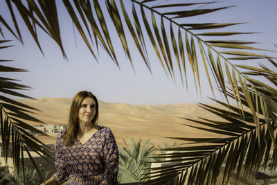 Portrait of young woman standing by palm trees