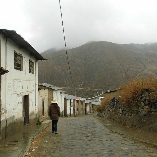 REAR VIEW OF A MAN WALKING ON VILLAGE IN MOUNTAIN