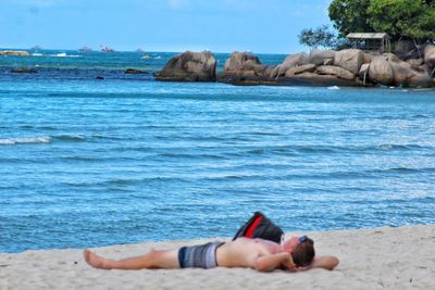 Man lying on rock in sea against sky