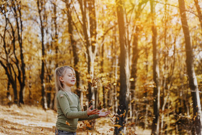 Small little child girl playing with leaves in forest. kid throws leaves up, they are falling down