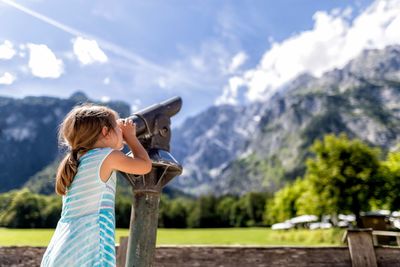 Girl looking through binoculars against mountains