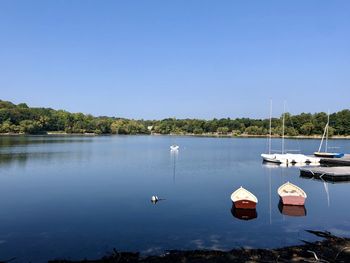 Sailboats moored in lake against clear blue sky