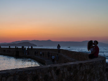 Couple kissing by sea against clear sky at dusk