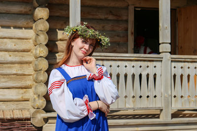 Portrait of young woman standing against wooden house 