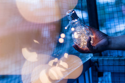 Cropped hand holding illuminated light bulb