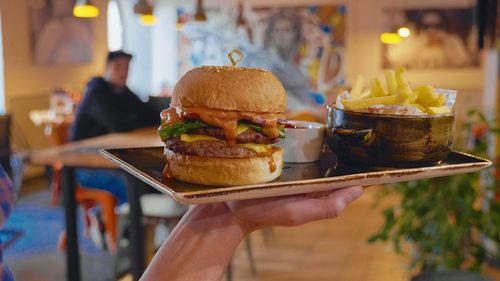 Cropped hand holding food in tray with man in background