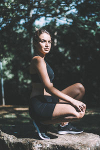 Portrait of young woman crouching on rock against trees