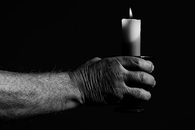 Close-up of hand holding candles against black background