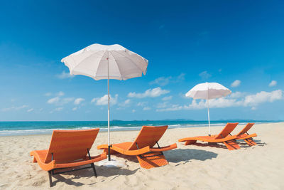 Deck chairs and parasols on beach against sky