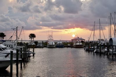 Boats moored at harbor against cloudy sky