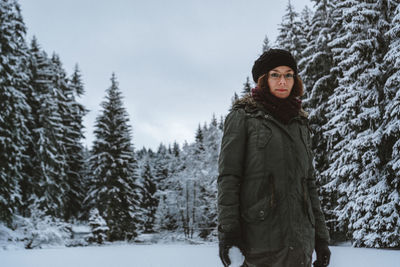 Portrait of young woman standing against trees during winter