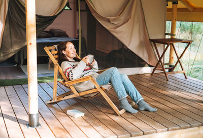 Brunette woman in nordic sweater drinking tea and relaxing in glamping in nature