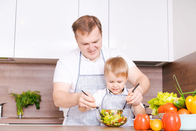 Happy family father with son preparing vegetable salad at home, vegetables