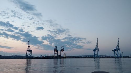 Cranes at commercial dock against sky during sunset