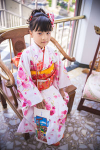 Cute girl in kimono sitting on chair at home