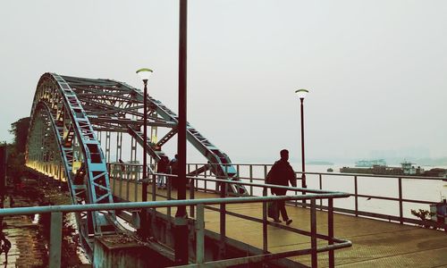 Man sitting on railing at amusement park against clear sky