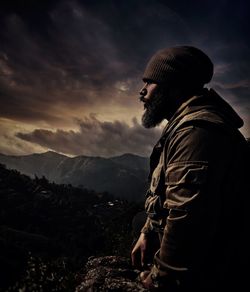 Side view of young man standing by mountain against sky