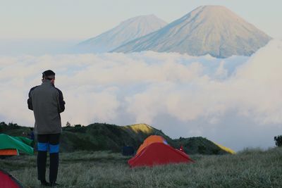 Rear view of man camping against mountains during sunset