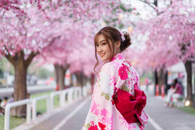 Portrait of smiling woman standing by pink flowers