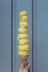 Hand holding ice cream against wall too many yellow colored  ice cream cone on a sunny day