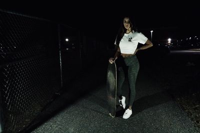 Full length portrait of young woman standing in illuminated city