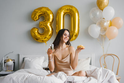 Cute woman holds a festive cake in her hands while sitting on the bed in the bedroom decorated
