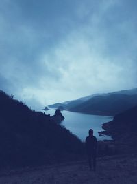 Rear view of silhouette man standing on mountain against sky