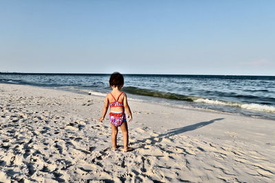 Rear view of girl standing at beach against clear sky