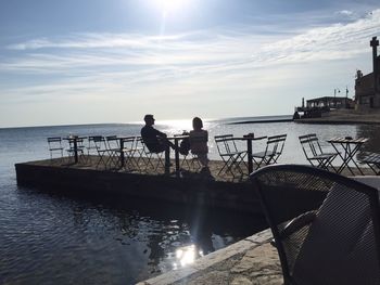 Friends sitting on chairs against sea at beach cafe