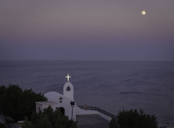 Illuminated cross on chapel by sea against sky at dusk