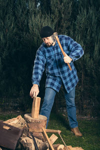 Full length of lumberjack chopping wood from axe against trees at forest