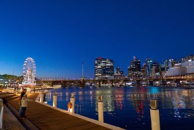 Illuminated buildings in city against clear blue sky