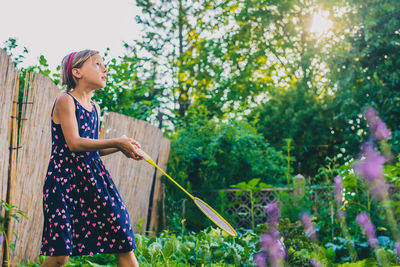 Side view of girl playing badminton against trees in yard