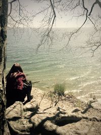 Woman sitting on bare tree against sky