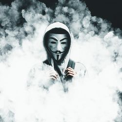Portrait of young woman holding mask against sky