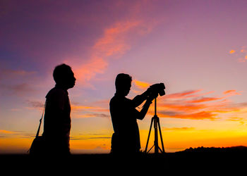 Silhouette men photographing against sky during sunset