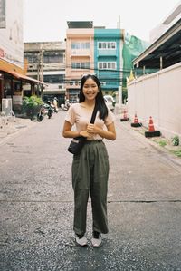 Portrait of smiling young woman standing on street in city