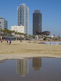 People at beach in city against clear sky