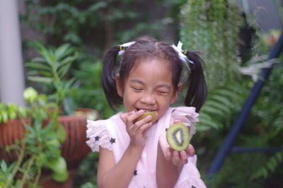 Close-up of smiling girl holding kiwi against plants