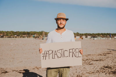 Portrait of smiling man wearing hat holding poster standing on beach