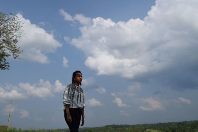 Young woman standing on field against cloudy sky