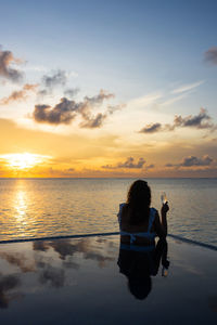 Attractive woman on a infinity pool near the ocean with a glass of champagne.back view