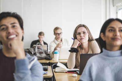 Young woman with friends listening while sitting in classroom